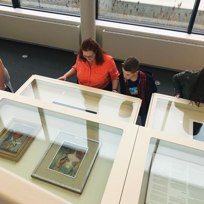 A woman and a boy study framed paintings in a museum display case.