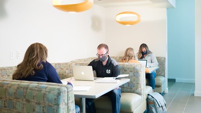 Students study on laptops while wearing COVID-19 masks.