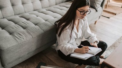 woman sitting on a floor, taking notes in a book.
