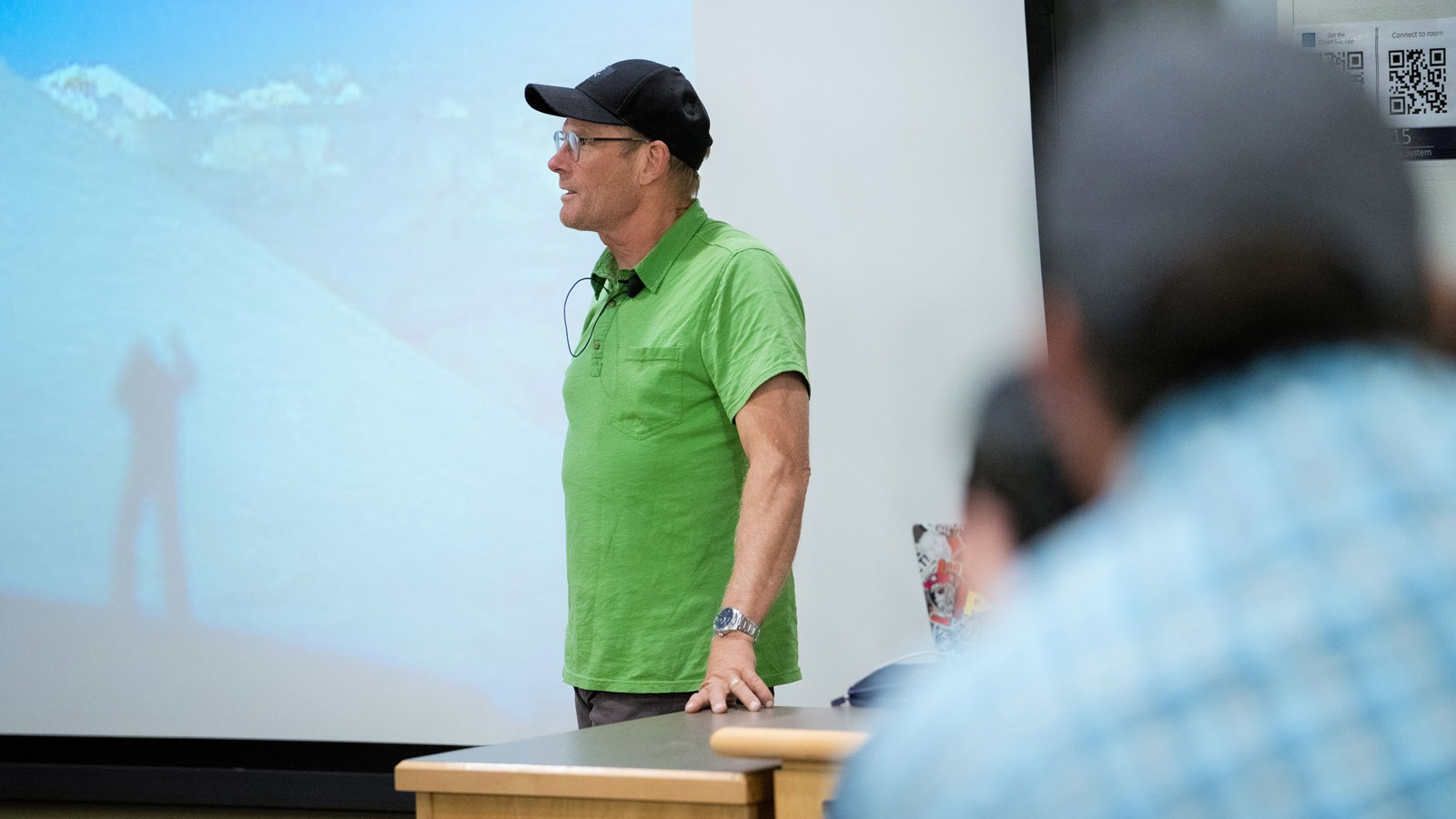 A man speaks in front of a mountaineering slideshow.