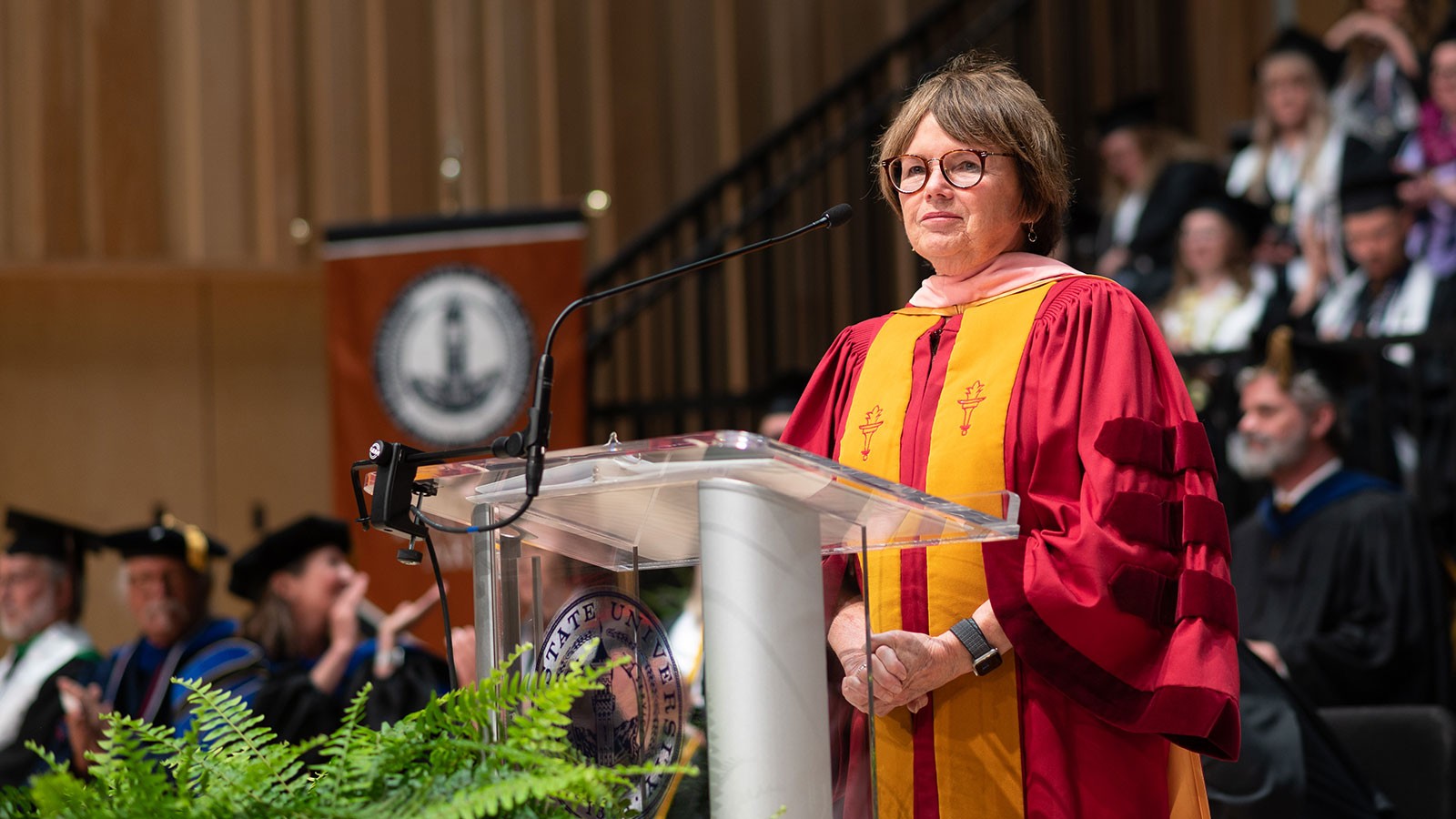 Rachel Nardo stands at the lectern at the Caine College of the Arts convocation ceremony.