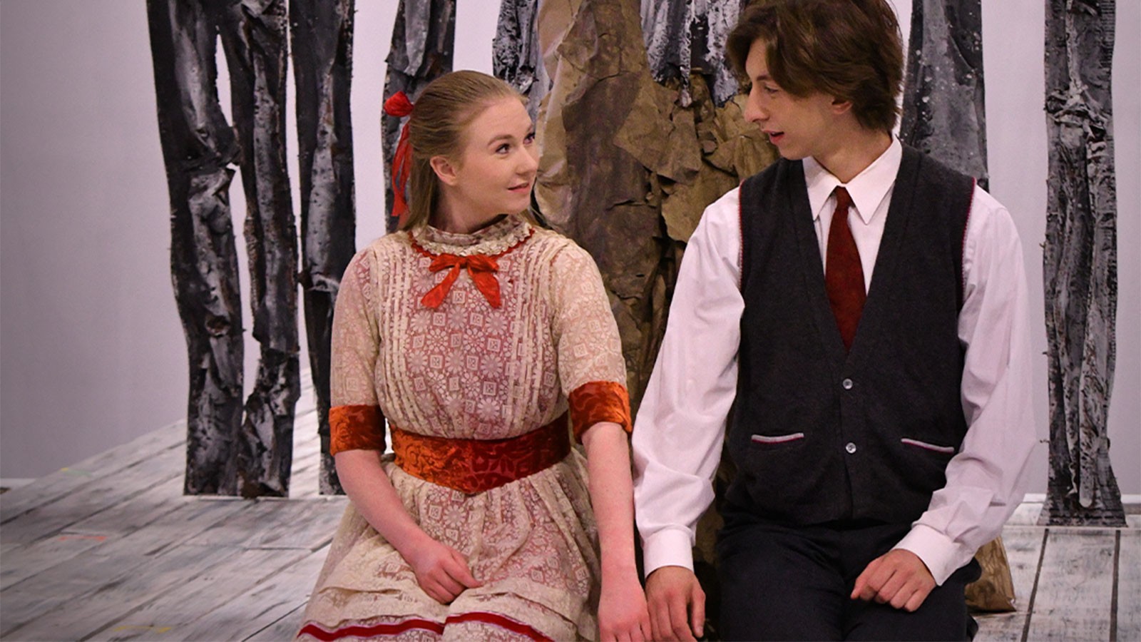 Two actors kneeling and holding hands on stage.