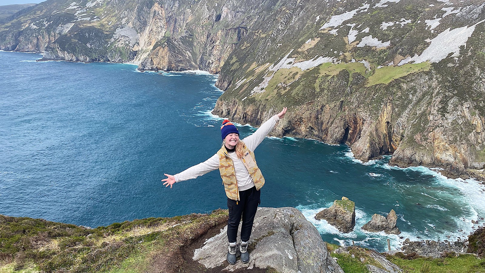 A woman holding out her arms on a mountain overlooking the sea.
