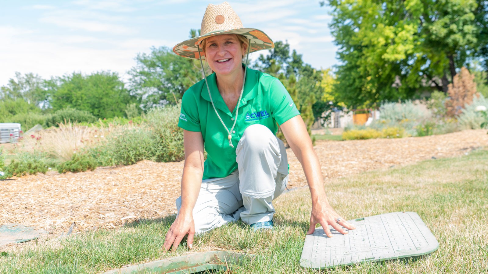 Kelly Kopp kneels by a water valve box on a lawn.