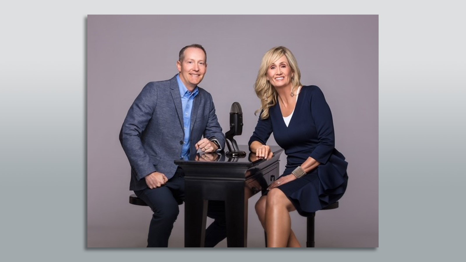 Dave Schramm and Liz Hale posing next to a podcast microphone.