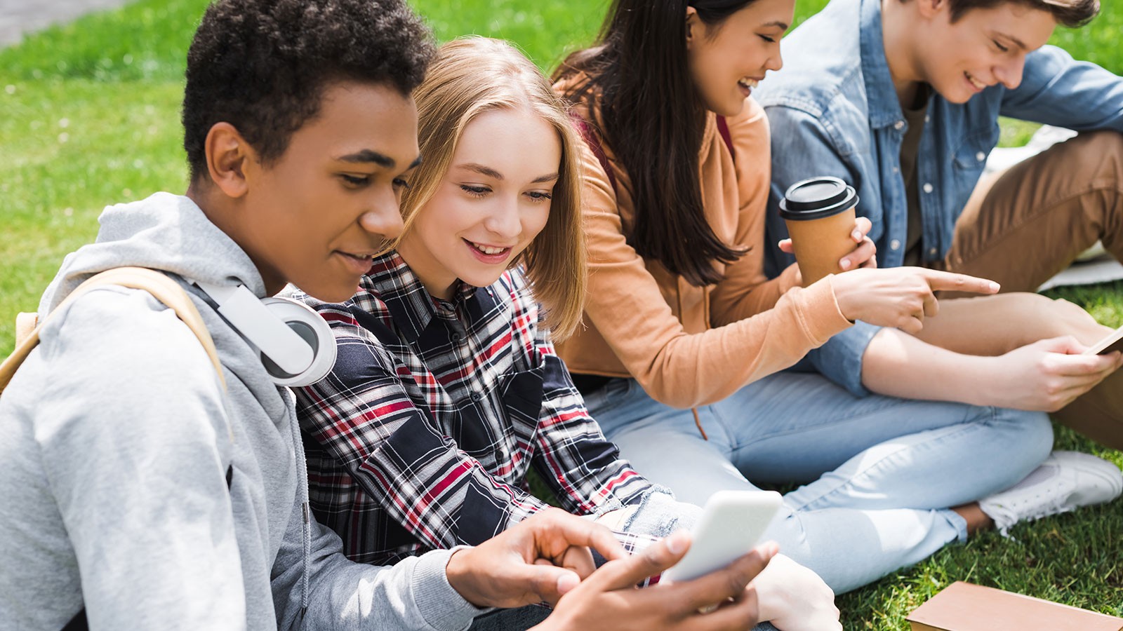 Teens use cell phones while sitting on the grass.