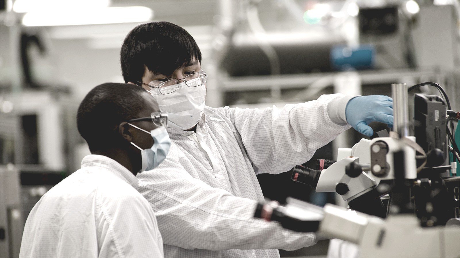 Two people in personal protective equipment operate machinery.