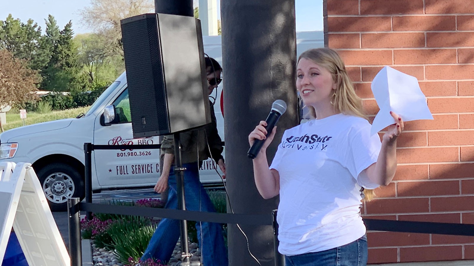 Bailey Lundquist holds a microphone as she speaks outdoors.