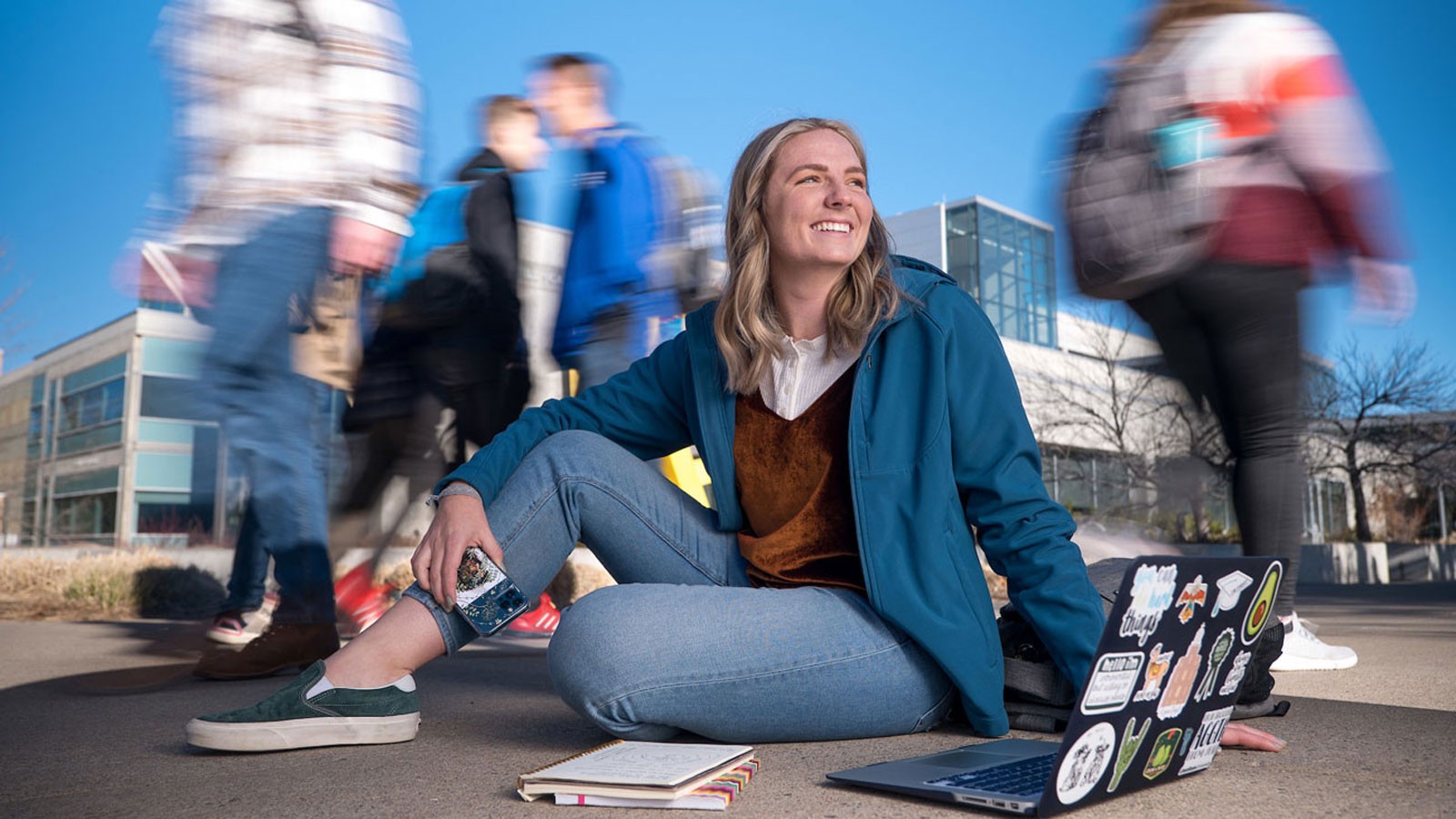 A woman sits on the sidewalk with a laptop and notebooks in this photo illustration.