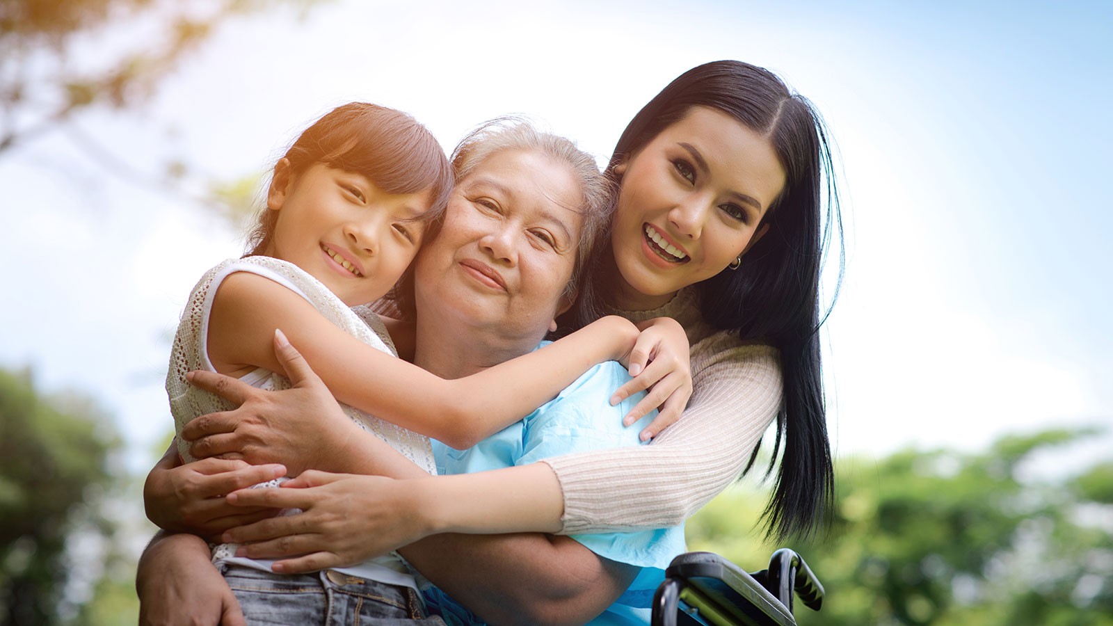 Two people hug a person sitting in a wheelchair.
