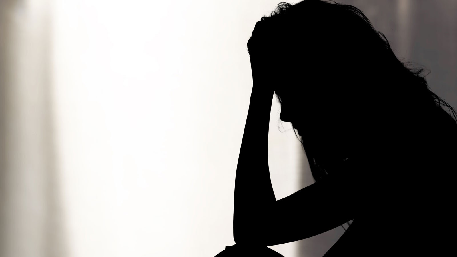 A silhouetted woman rests her forehead on her hand in distress.
