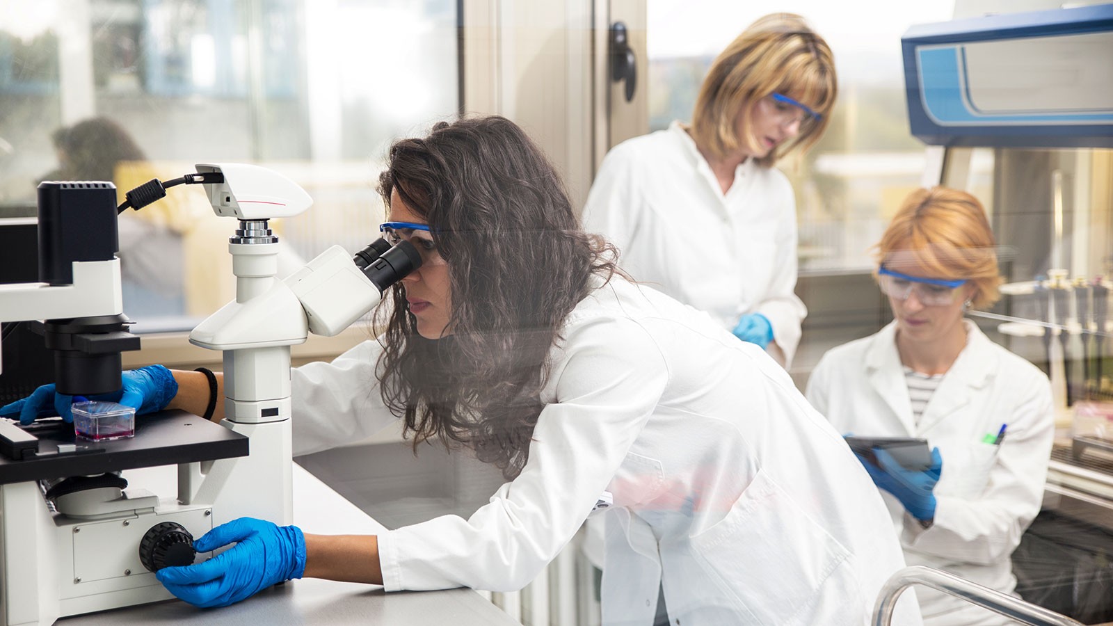 A woman in a lab coat looks into a microscope.