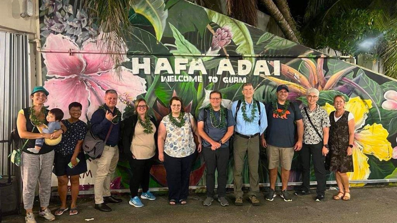 People posing in front of a "welcome to Guam" sign.