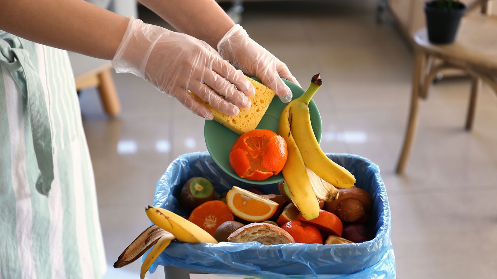 A person scraping fruit peels into a compost bin.