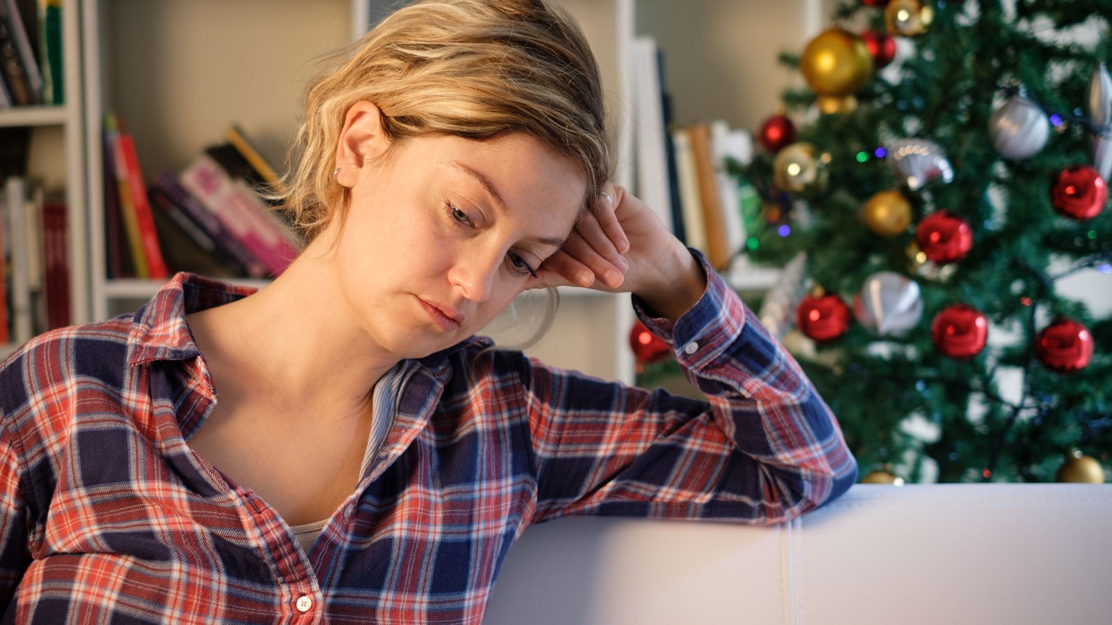 A woman looking worried in front of a Christmas tree.