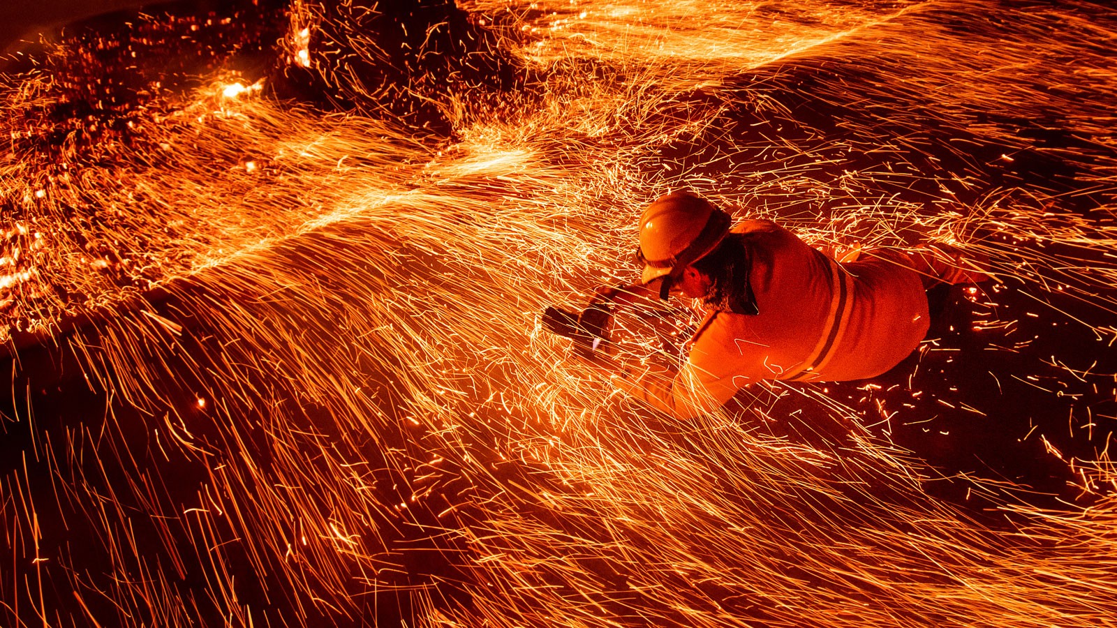 A person taking a photograph amid sparks from a wildfire.