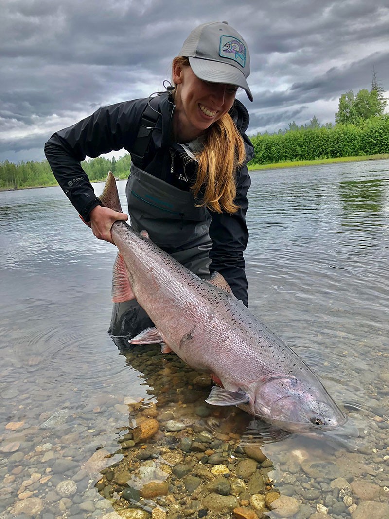 A woman wading in a river holds a fish.
