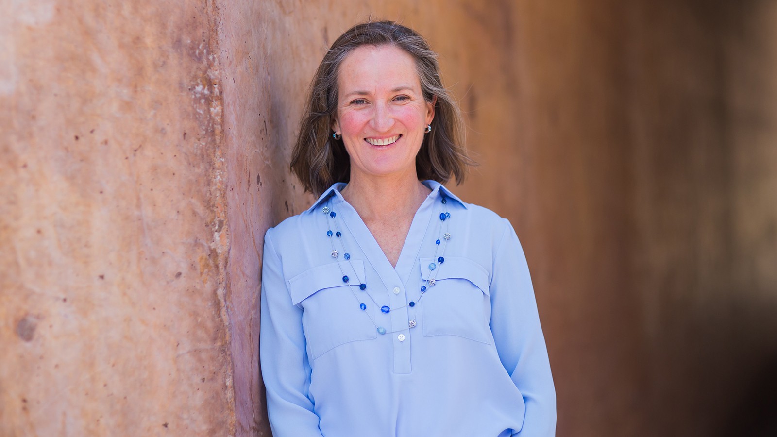 A woman poses for a photo against a stone wall.