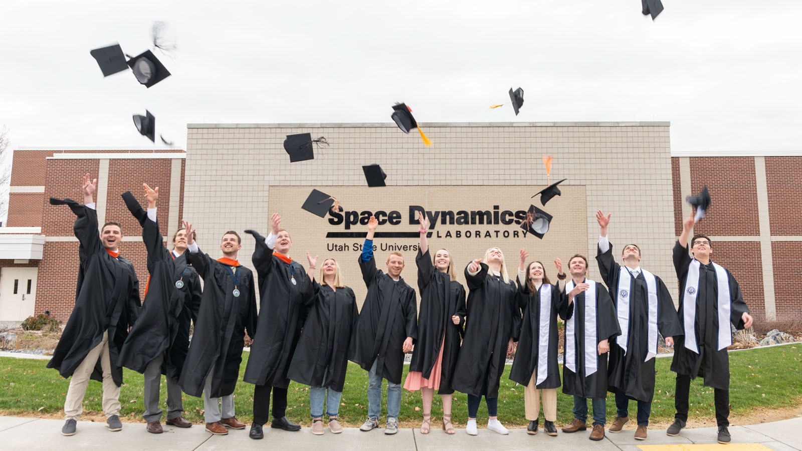 Students throwing mortarboards in the air outside an SDL building.