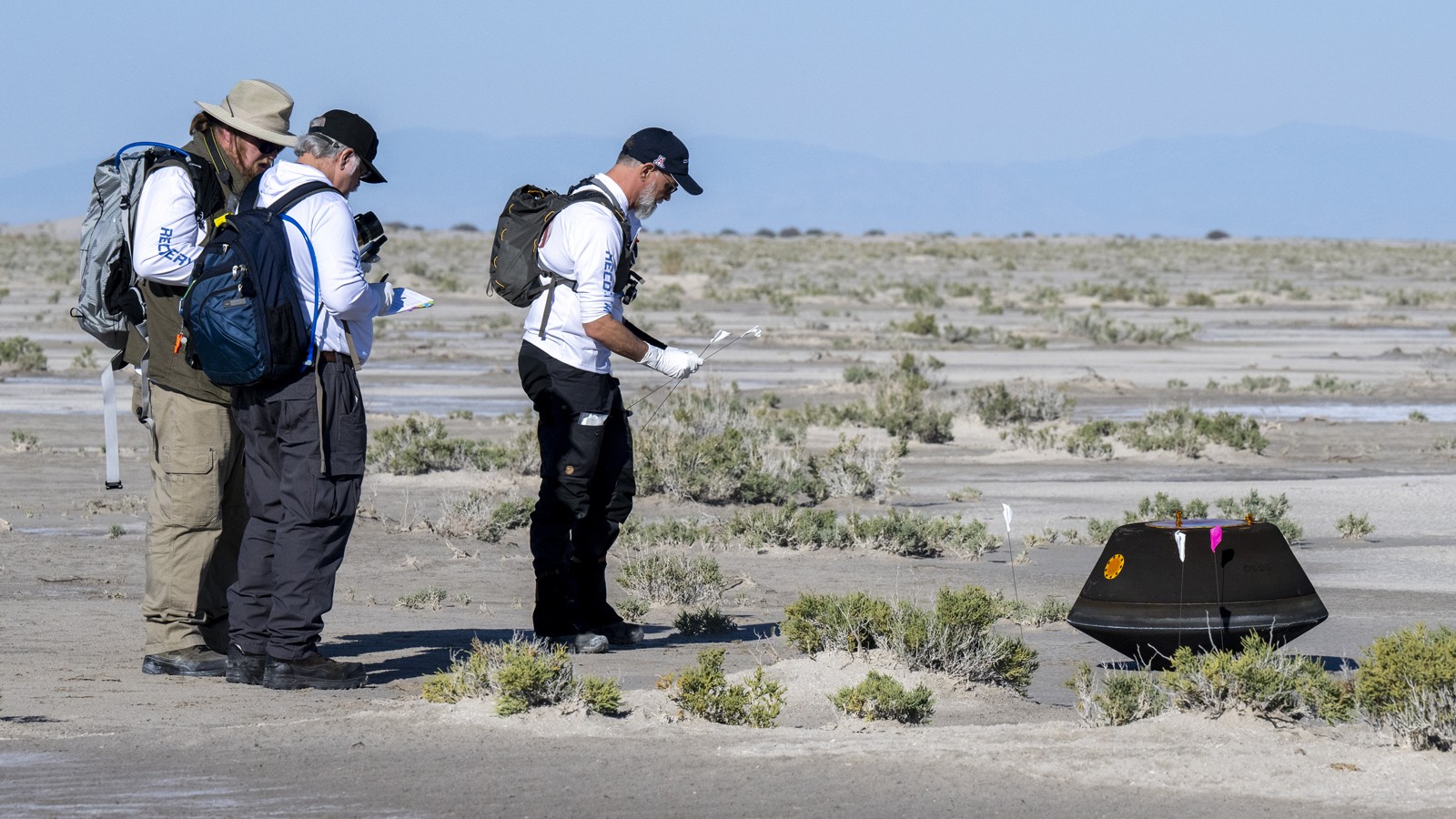 Scientists examining a small, landed space exploration capsule.