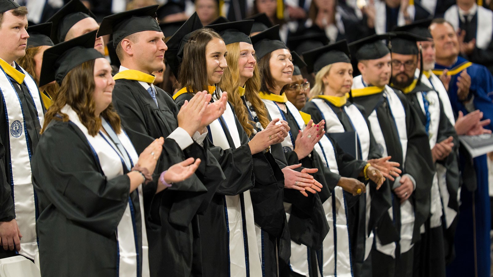 People in commencement robes applauding.