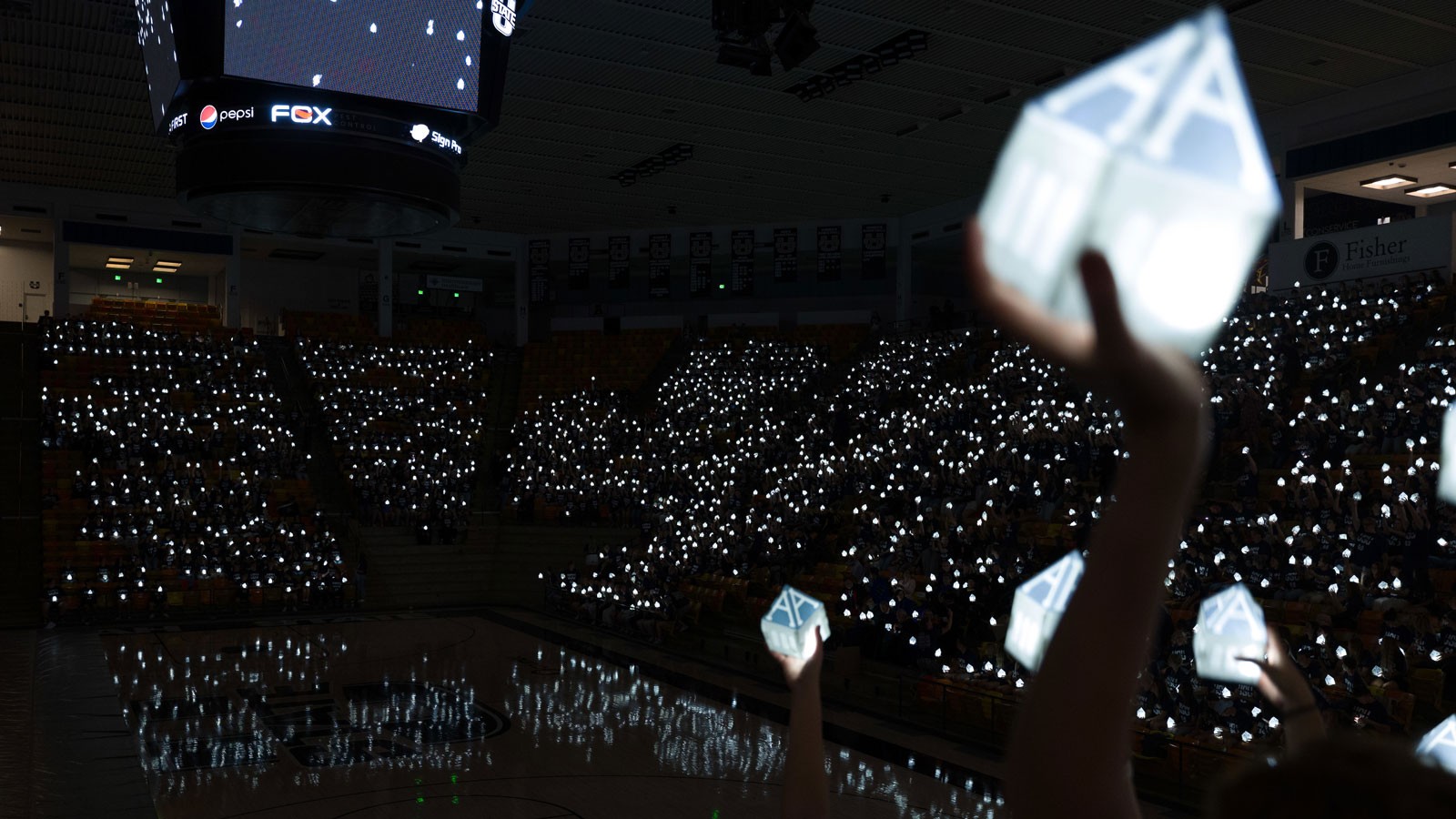 People in a stadium holding A-shaped lanterns.