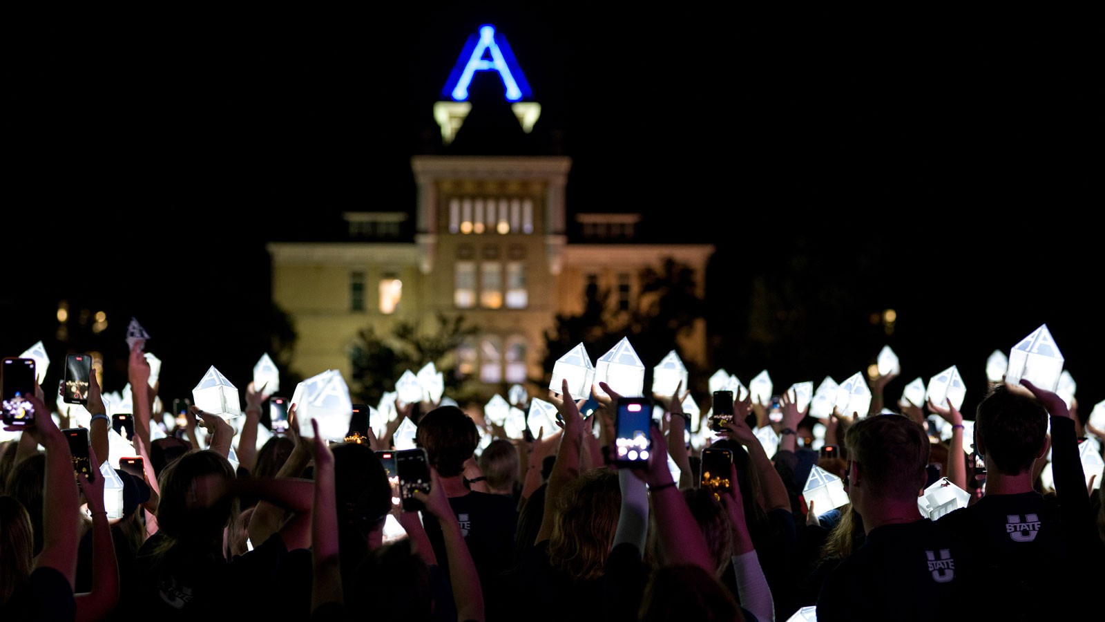 Students hold lanterns shaped like Old Main's tower in front of Old Main.