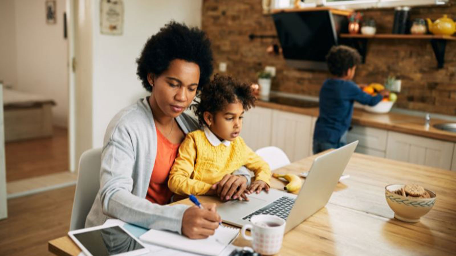 A mother using a computer while tending two children.