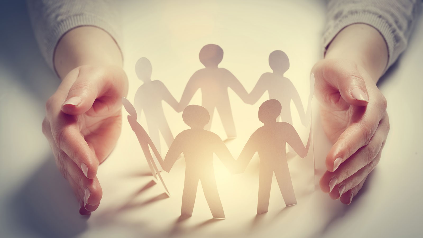A photo illustration of a circle of paper dolls between two hands.