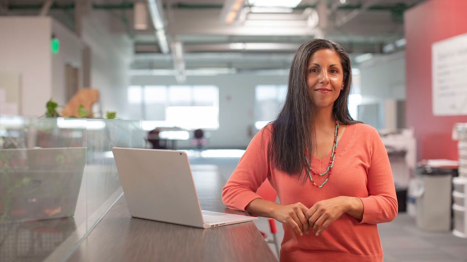 A woman standing at a laptop in an office.