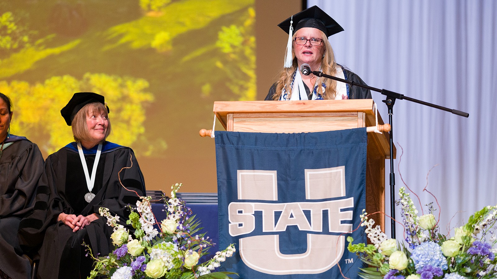 A student in graduation regalia gives a speech.