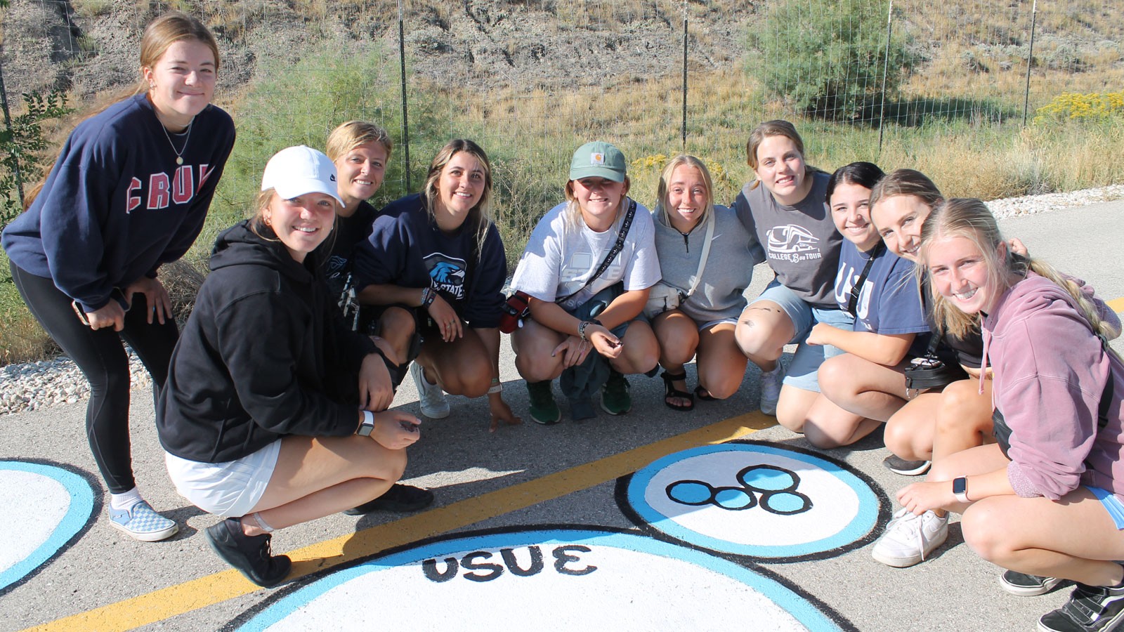 People gather around a street painting that says "USU E."