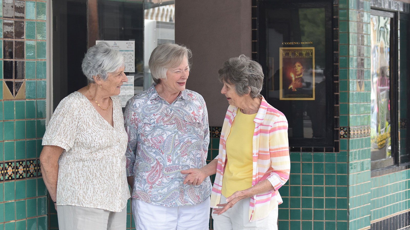 Women speaking by a movie theater box office.