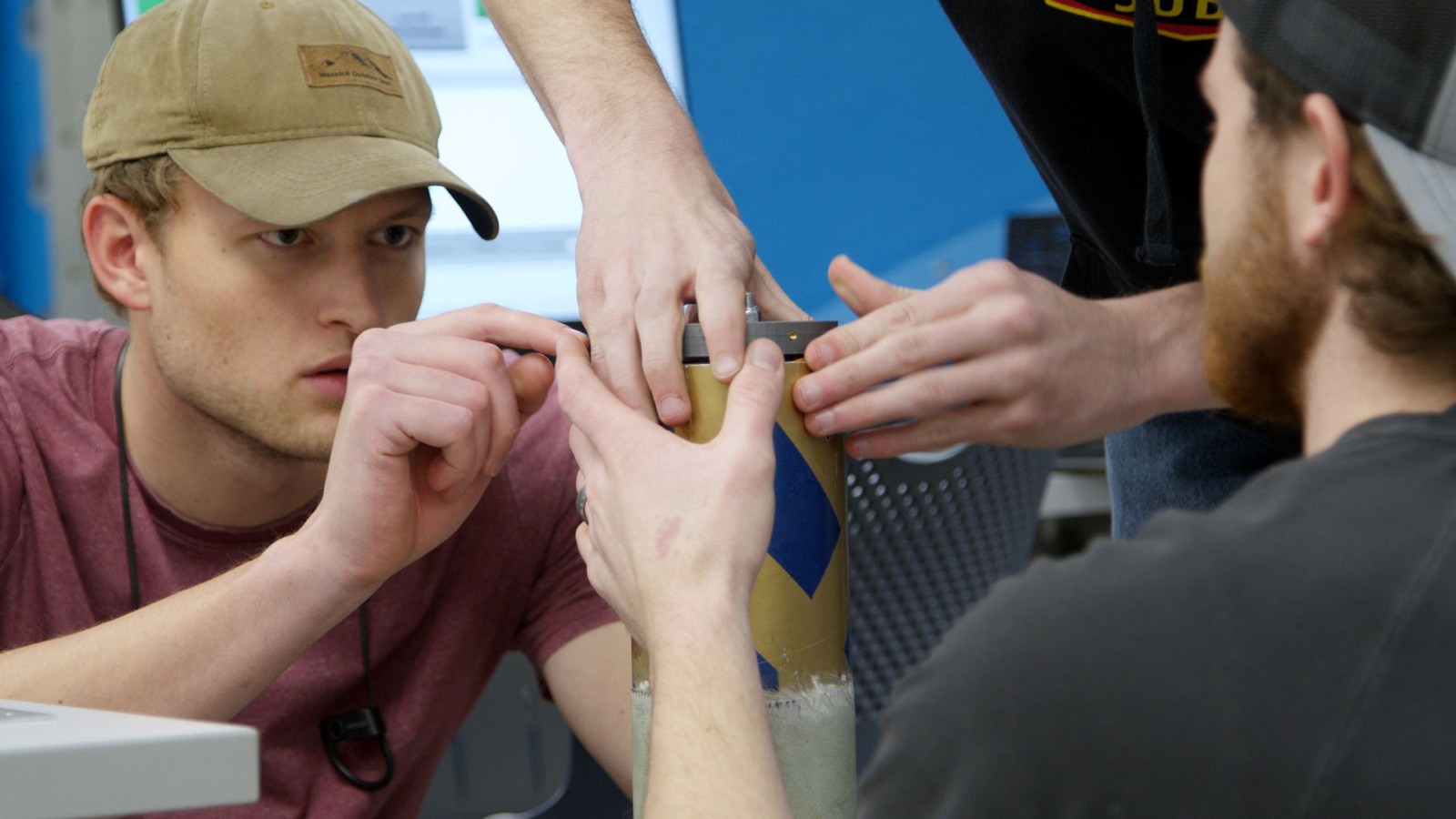 A male student in a hat works on a rocket control.