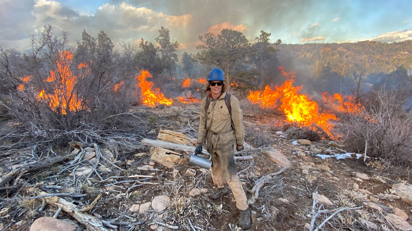 A worker poses in front of burning slash piles.