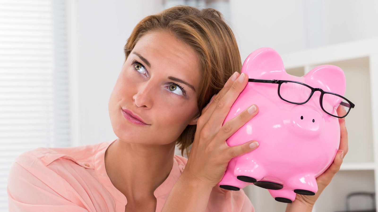 A woman putting her ear to a piggy bank.