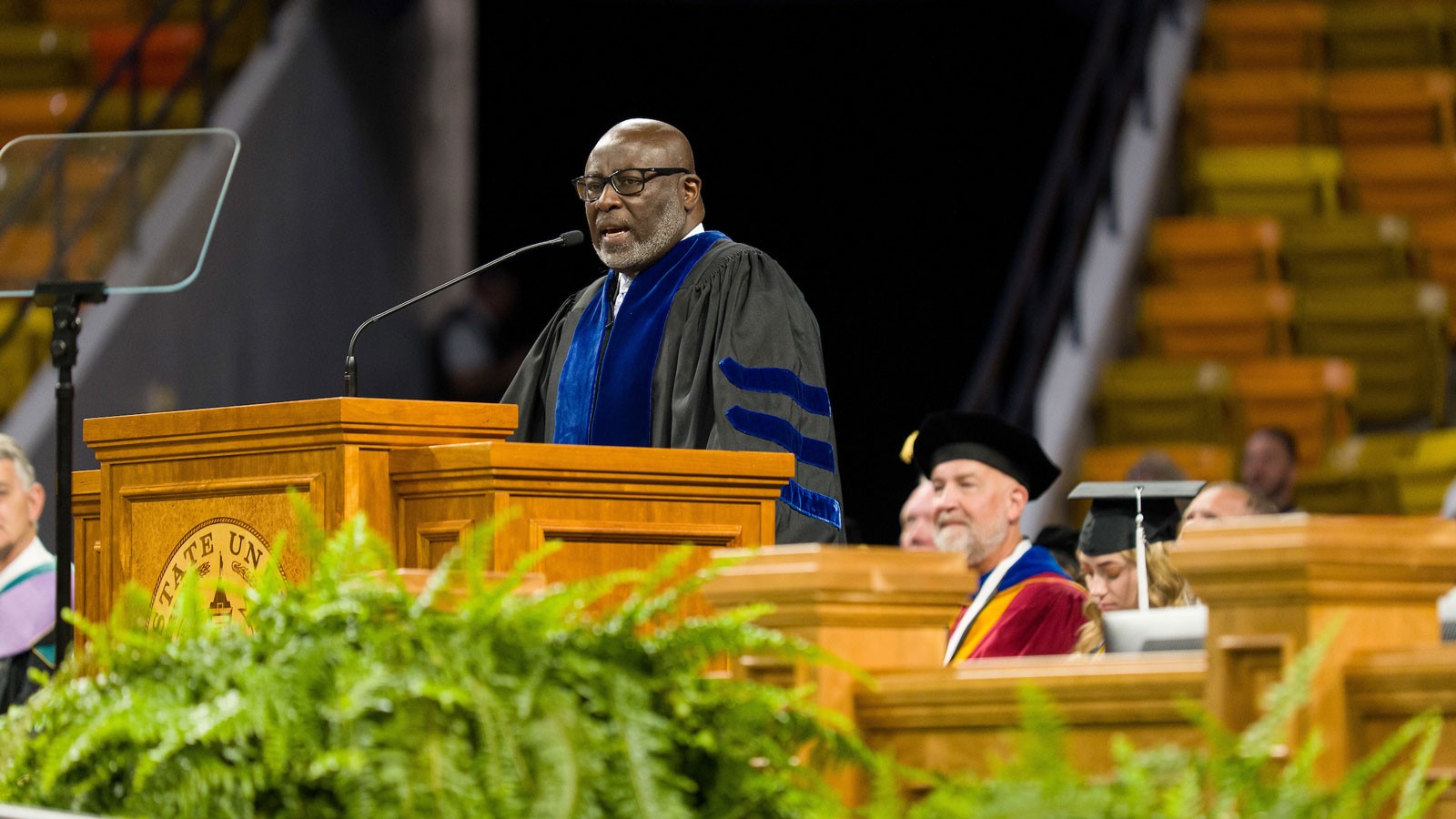Paul Jones wearing graduation clothing and speaking at a rostrum.