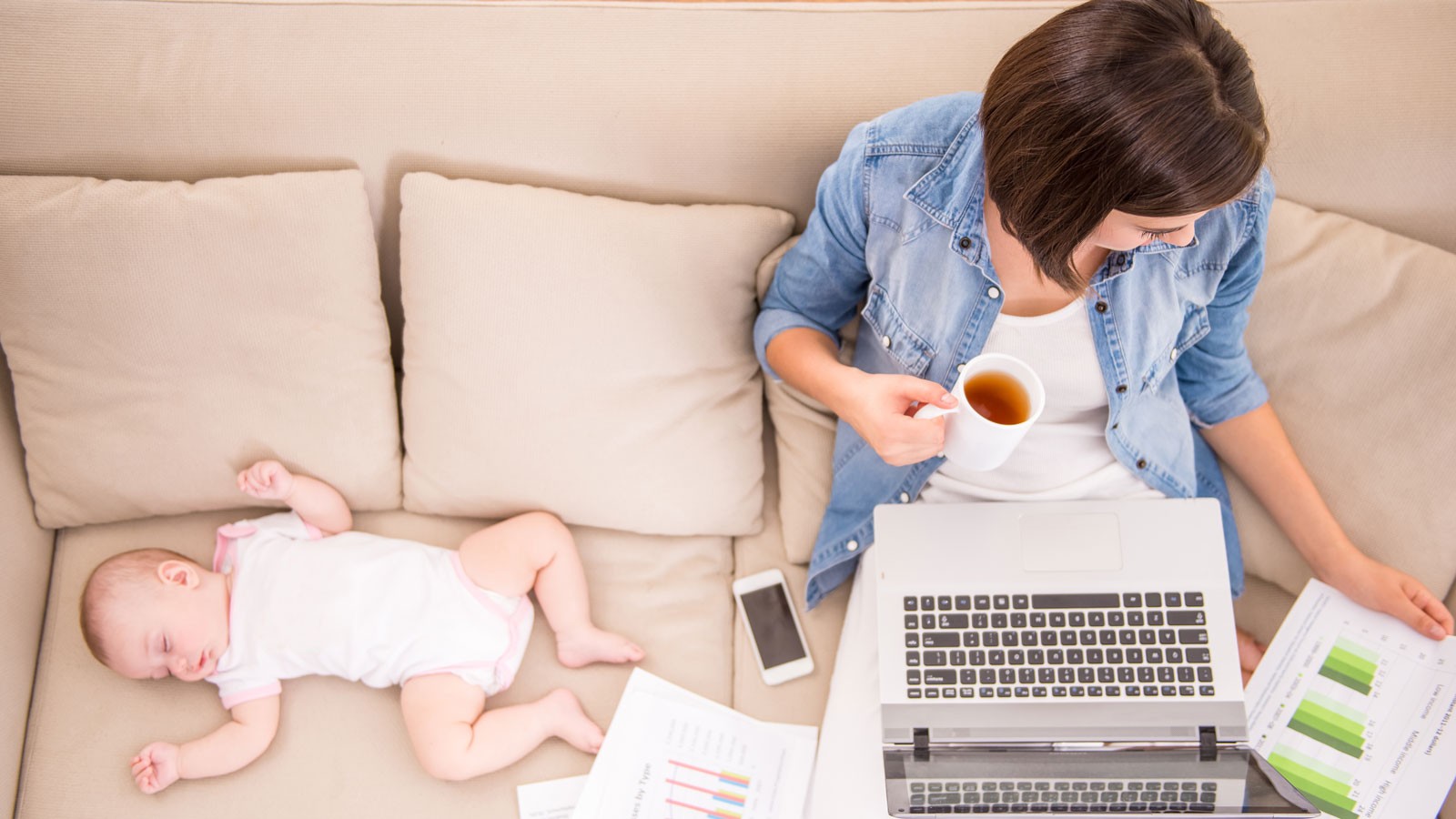A person working on a laptop next to a napping infant.