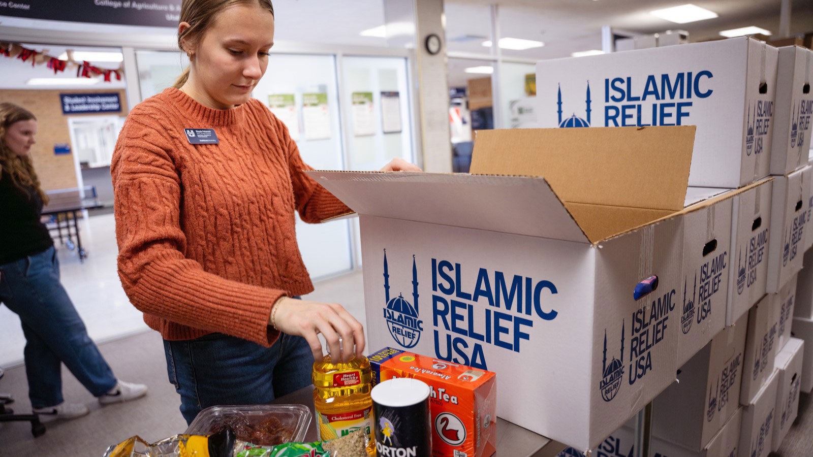 A volunteer packing food into a cardboard box that says "Islamic Relief USA."