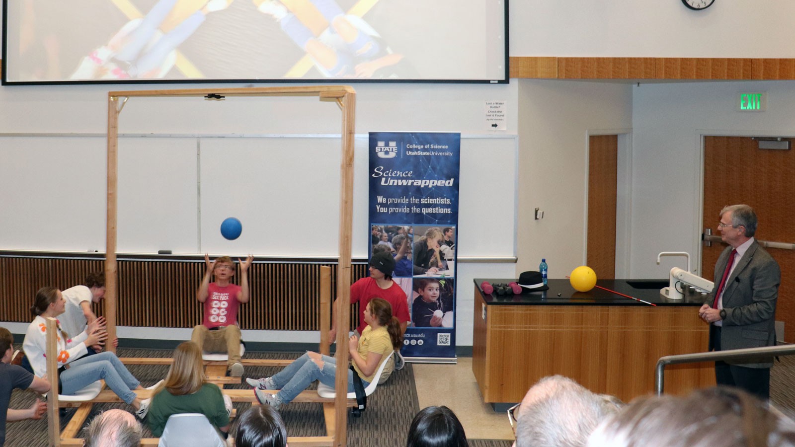 People demonstrating science using a wooden carousel in a classroom.