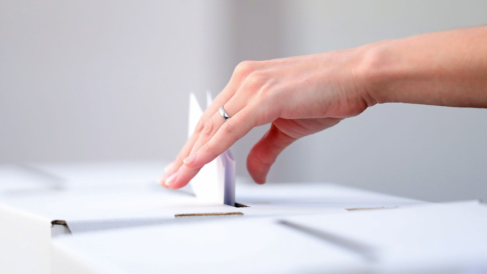 A hand dropping a ballot into a box.