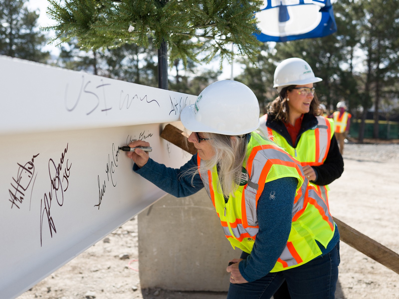 A woman signs her name to a steel beam while wearing construction gear.