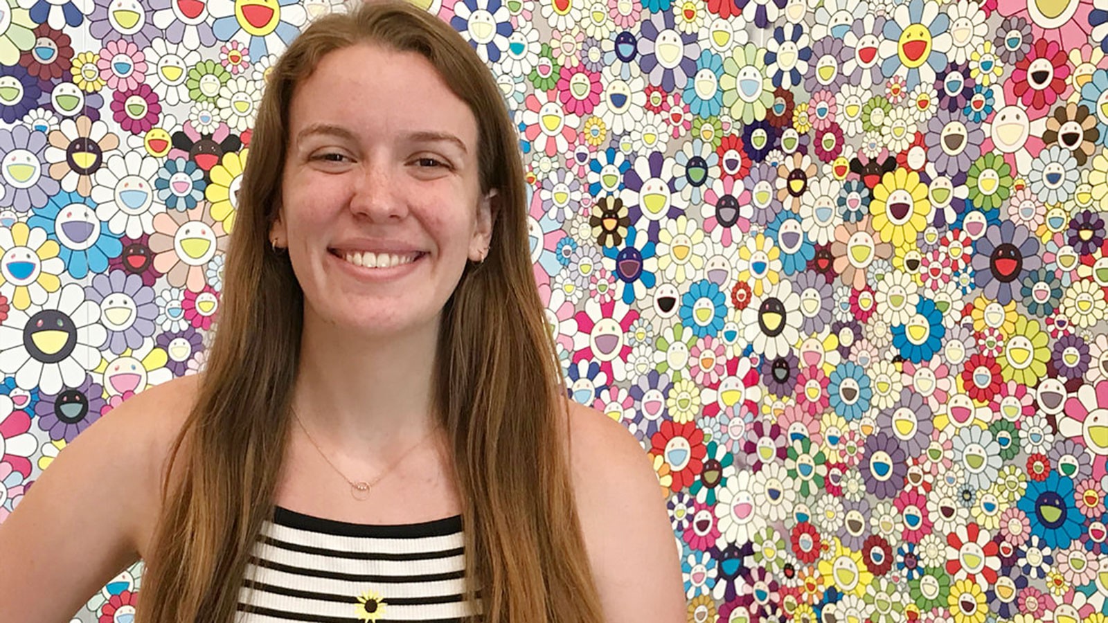 Julie Petersen poses for a photograph in front of a backdrop of colorful, smiling cartoon flowers.