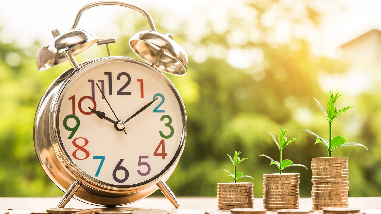 An alarm clock sits by growing stacks of coins sprouting plants.