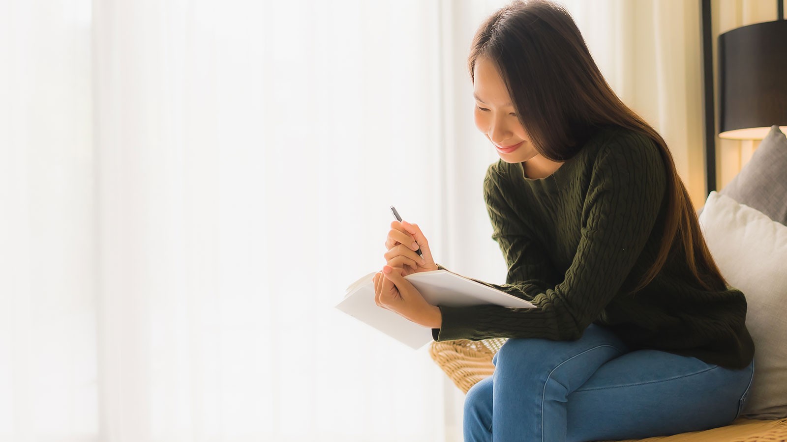 A person sits on a couch and writes in a notebook.
