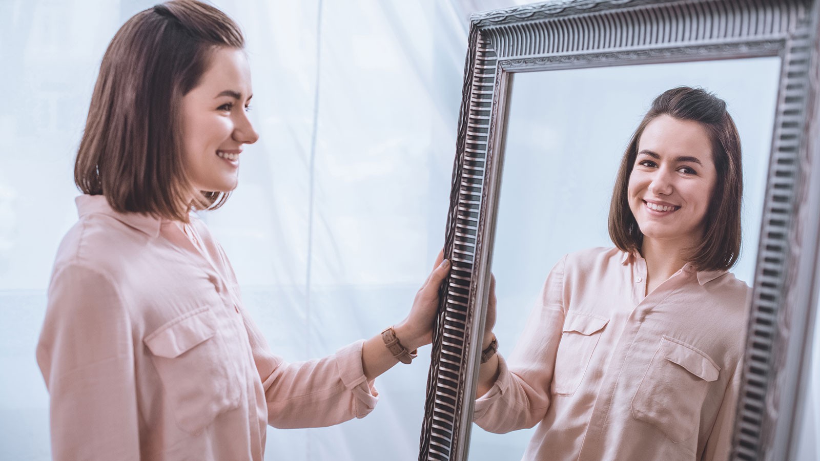 A woman smiles as she looks at her reflection in the mirror.