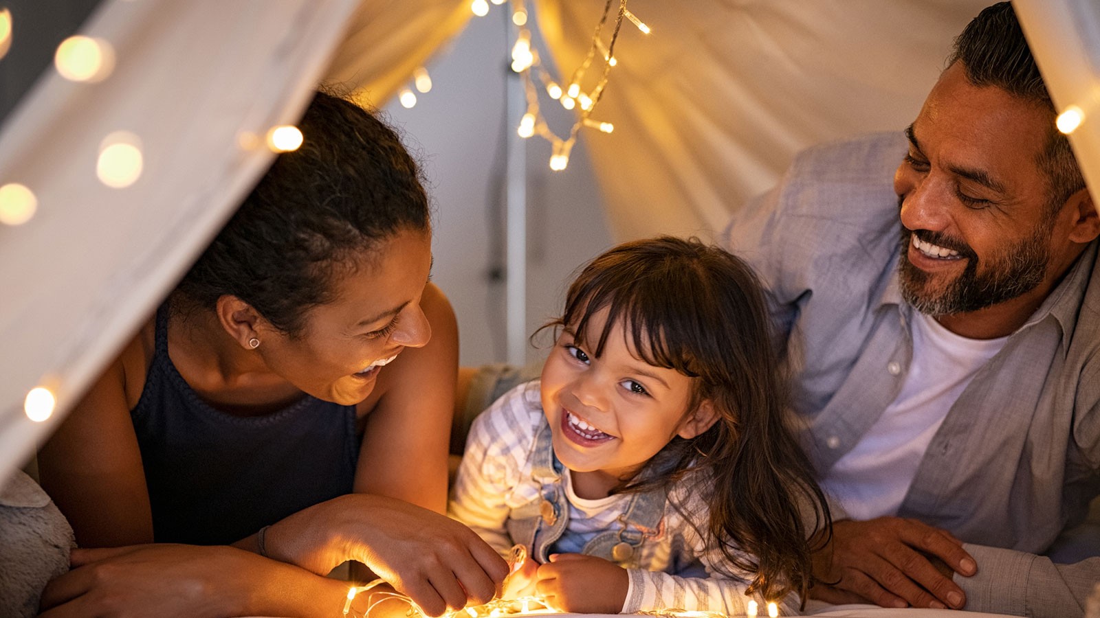 Mother and father snuggle in a tent with their daughter.