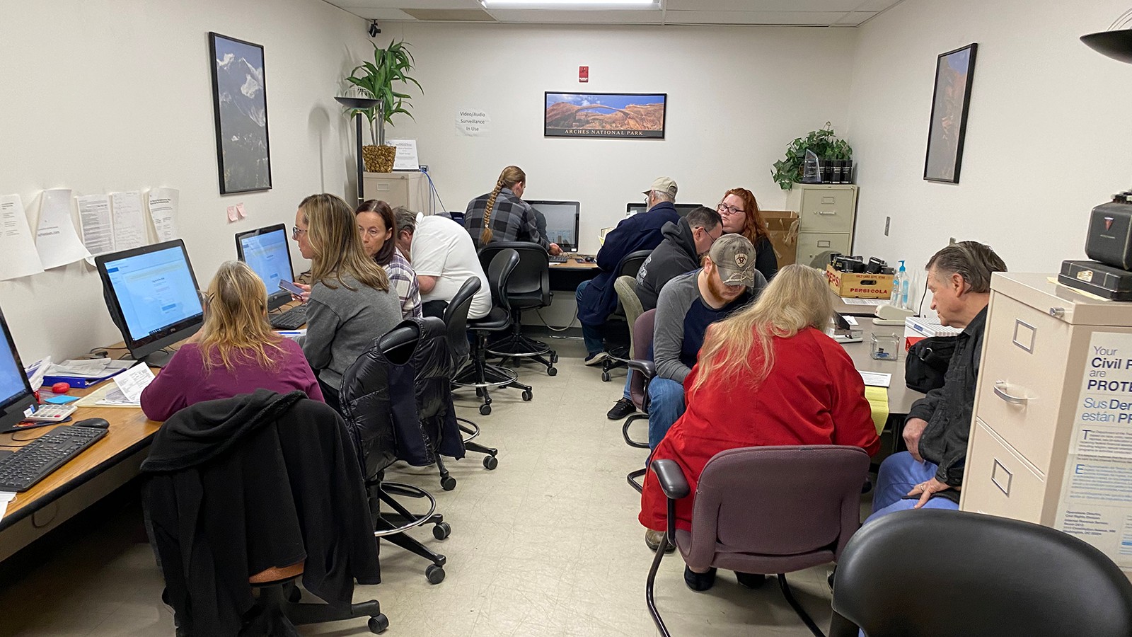 Multiple people sit around desks looking at computers and tax returns.