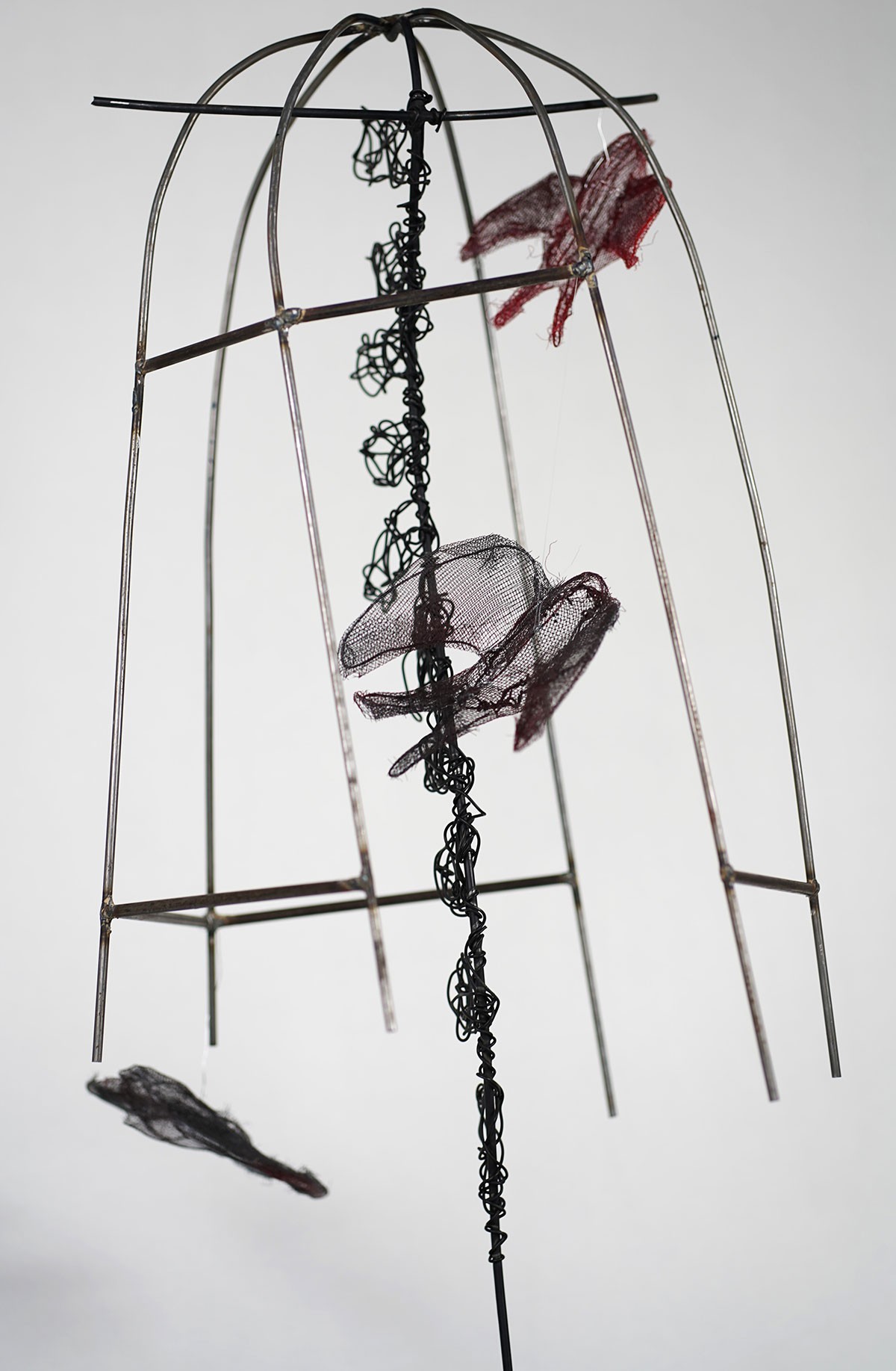 A sculpture. Metal bent in the shape of a birdcage with fabric birds inside.