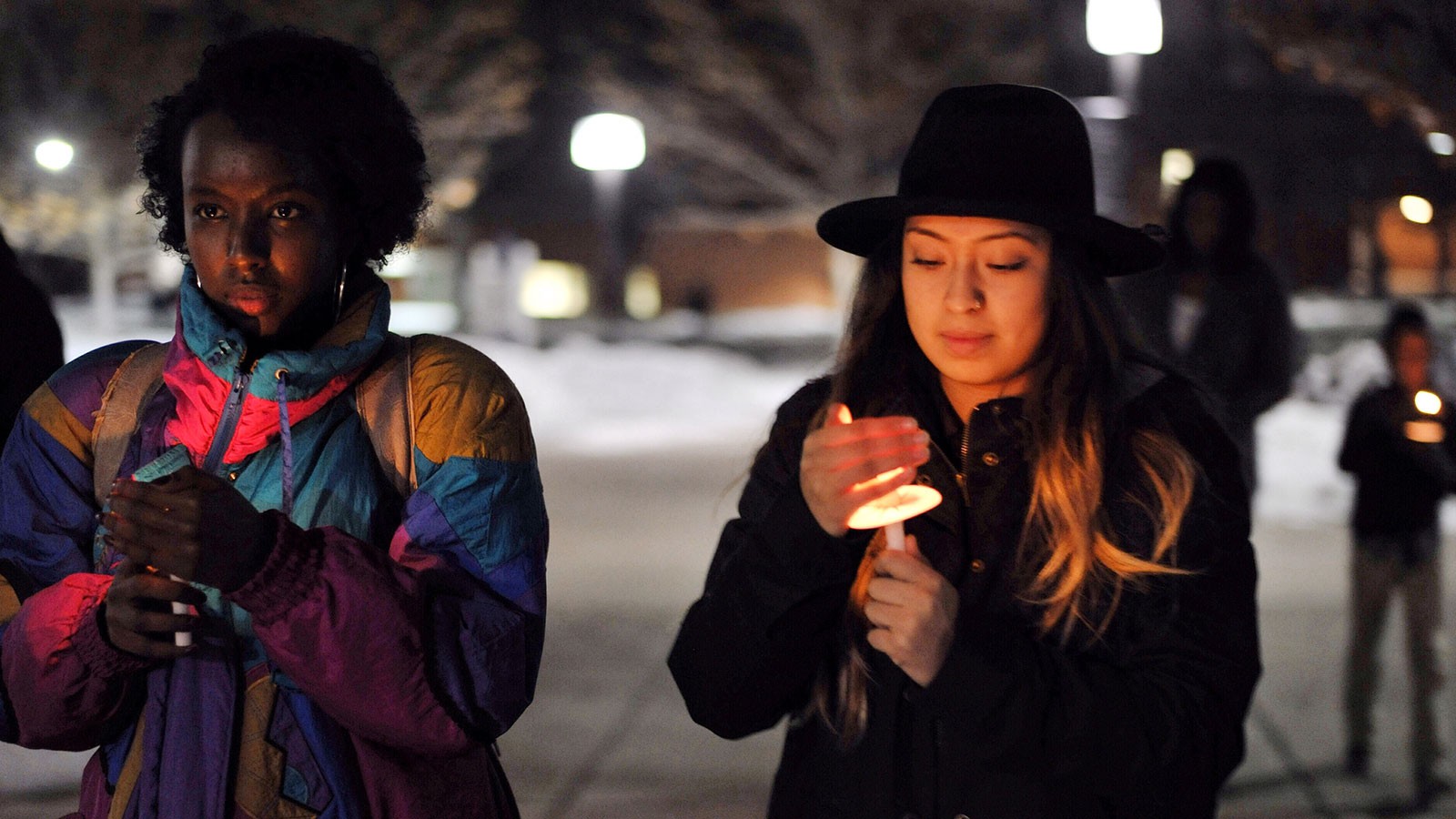 Students in coats shield candles from the wind on the USU campus.